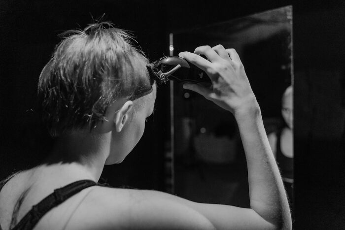 Person shaving head in front of mirror representing chaotic and dramatic breakup stories and emotional moments.
