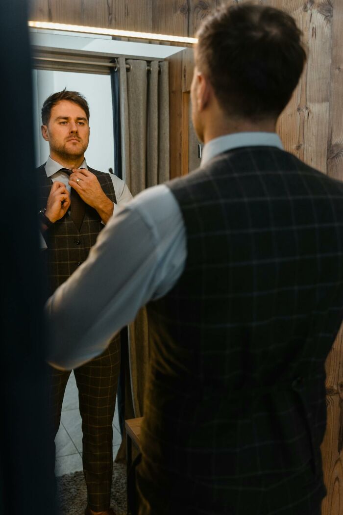 Man adjusting tie in mirror, reflecting on how spouses changed and red flags ignored after the wedding.