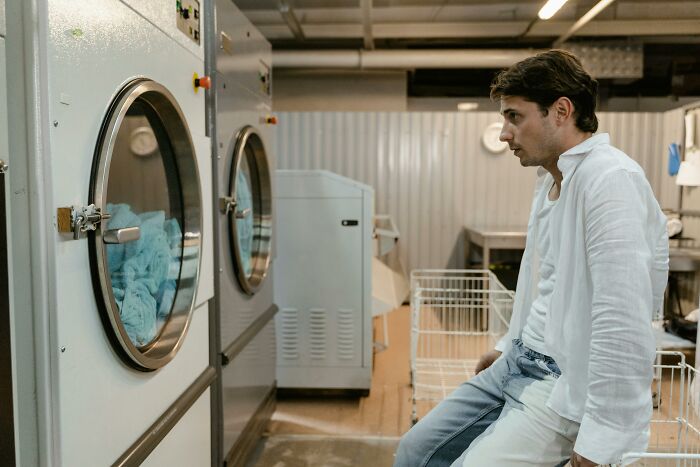A man sitting in a laundromat looking upset, reflecting on chaotic and dramatic breakup stories shared by people.