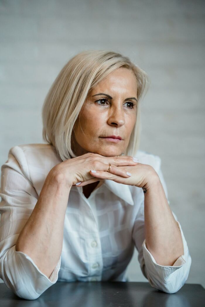 Older woman with blonde hair resting chin on hands, appearing thoughtful about secrets hidden from their partners.