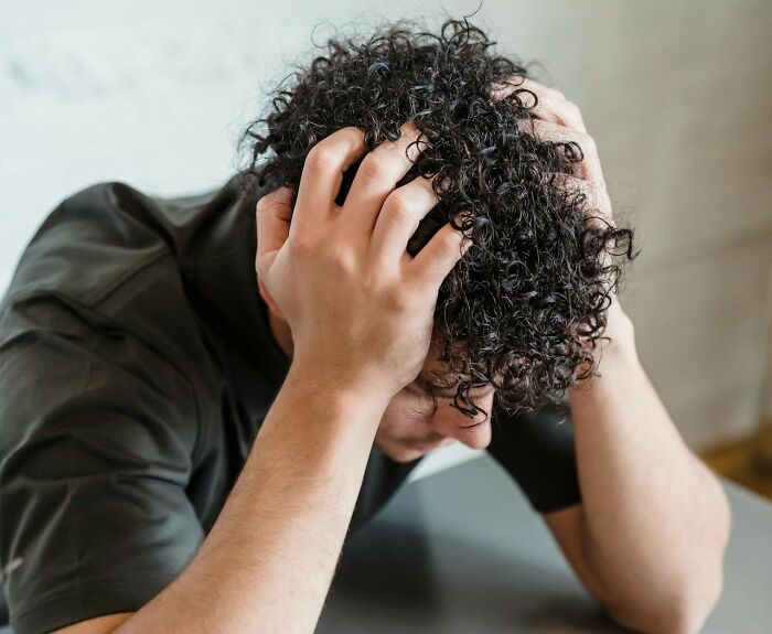 Man with curly hair holding his head in frustration after tattoo artists messed up a tattoo design indoors.