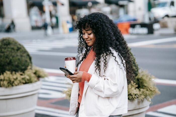 Woman holding coffee cup and phone smiling outdoors, representing advice from people with experience in online dating.