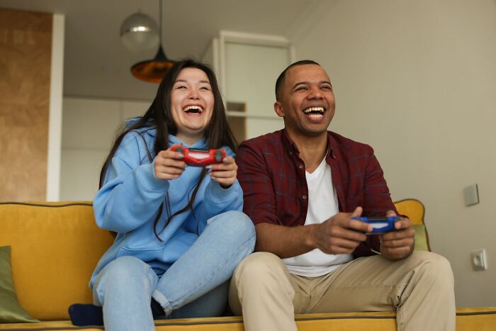 Young couple with experience in online dating laughing and playing video games together on the couch at home.