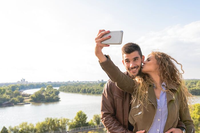 Couple taking a selfie outdoors by the river, depicting relationships and red flags spouses may show after the wedding.