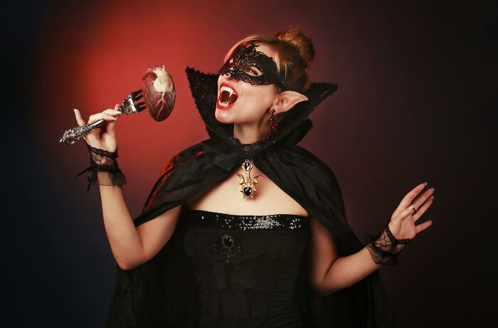 Young woman in vampire costume wearing a mask, holding a goblet with a prop heart, representing unique college courses.