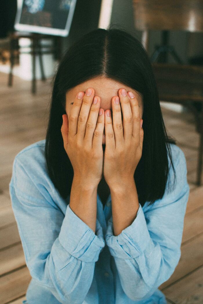 Young woman covering her face with hands indoors, symbolizing karma striking with zero mercy in emotional moments.
