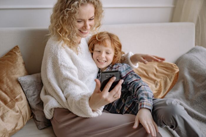 Woman and child smiling together while looking at a phone, representing advice from people experienced in online dating.