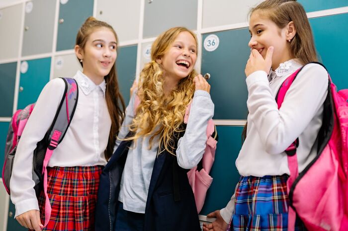Three school girls laughing and chatting by lockers, capturing a joyful moment of karma striking with zero mercy.