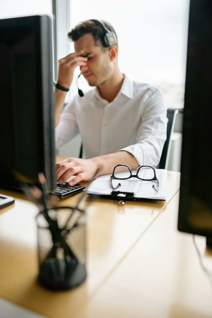 Stressed man wearing headset at computer, showing frustration and fatigue in a busy office environment with karma concept.