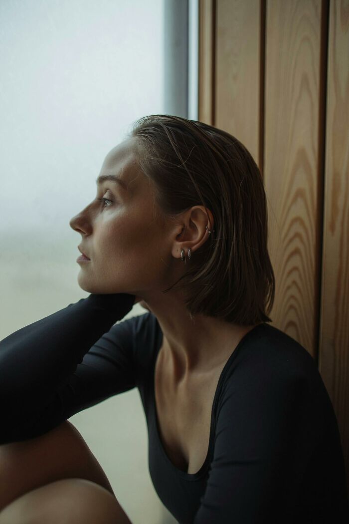 Young woman looking thoughtfully out a window, reflecting on disappointment in someone they idolized.