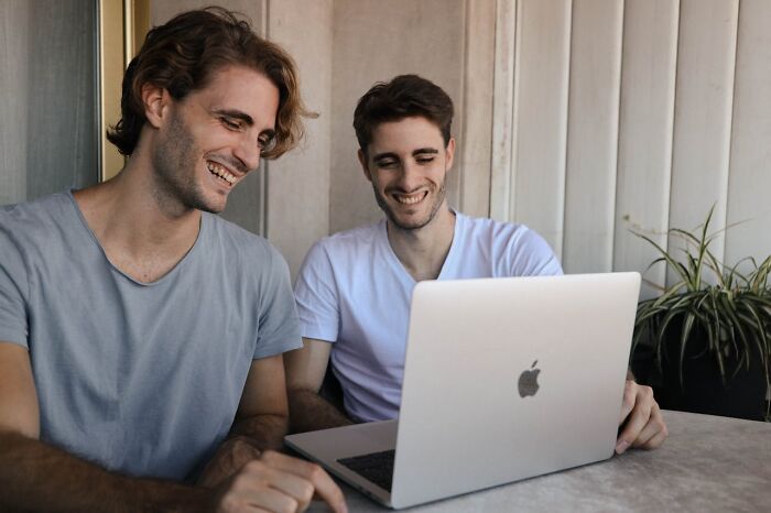 Two men smiling and looking at a laptop screen while discussing secrets people are hiding from their partners.
