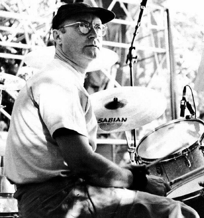 Black and white photo of a drummer playing a drum set during a live music performance on stage.