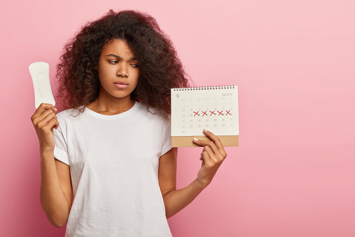 Young woman holding a sanitary pad and calendar with marked period days, representing period verification requirements.