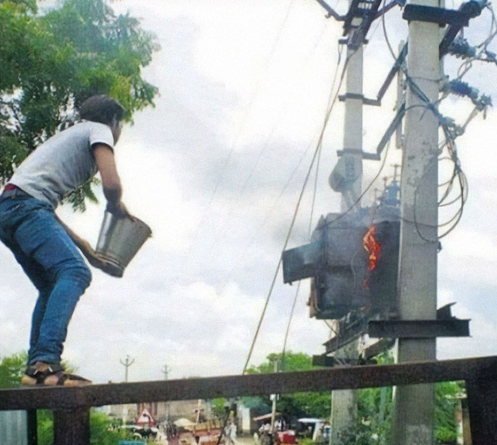 Man holding bucket near burning electrical transformer on pole, captured in hilarious photos before disaster struck.