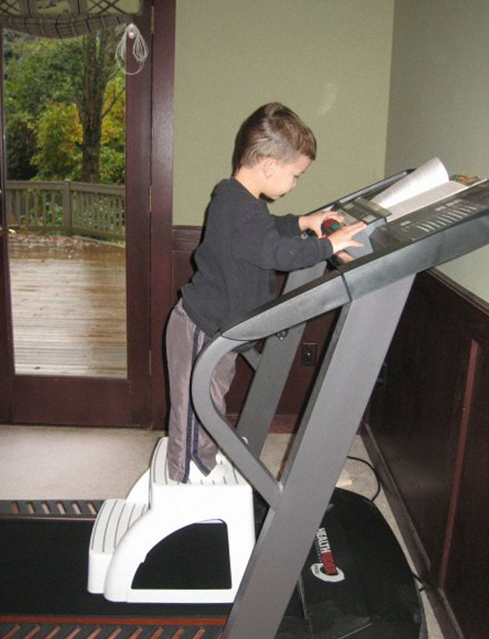 Young child standing on a step stool using a treadmill control panel in a hilarious photo before disaster struck.