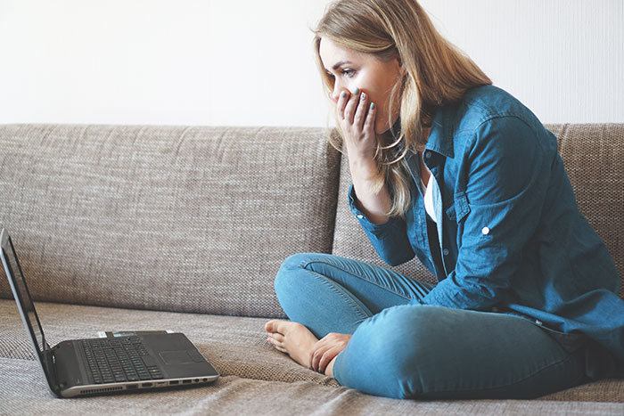 Woman in casual clothes looking shocked at laptop, representing educated person falling for scam investment debt. Woman in casual clothes looking shocked at laptop, representing educated person falling for scam investment debt.