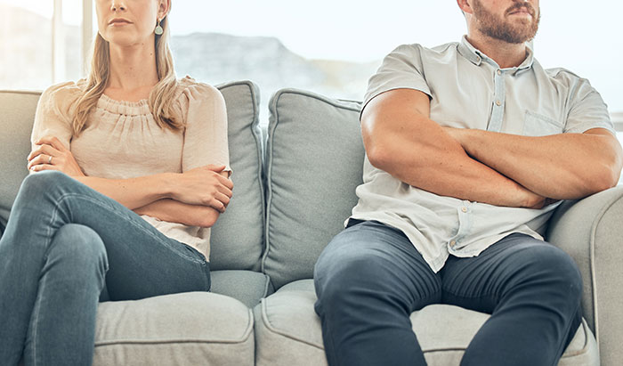 Couple sitting apart on a couch looking frustrated after one falls for scam investment causing debt and zero savings. Couple sitting apart on a couch looking frustrated after one falls for scam investment causing debt and zero savings.