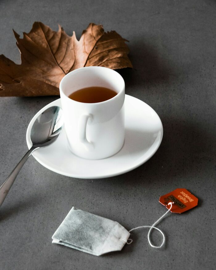 White cup of tea on a saucer with a spoon and a tea bag, styled with autumn leaves, illustrating embarrassing moments.