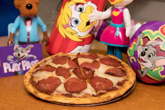 Pepperoni pizza on a table with colorful toys and a play pass card in the background.