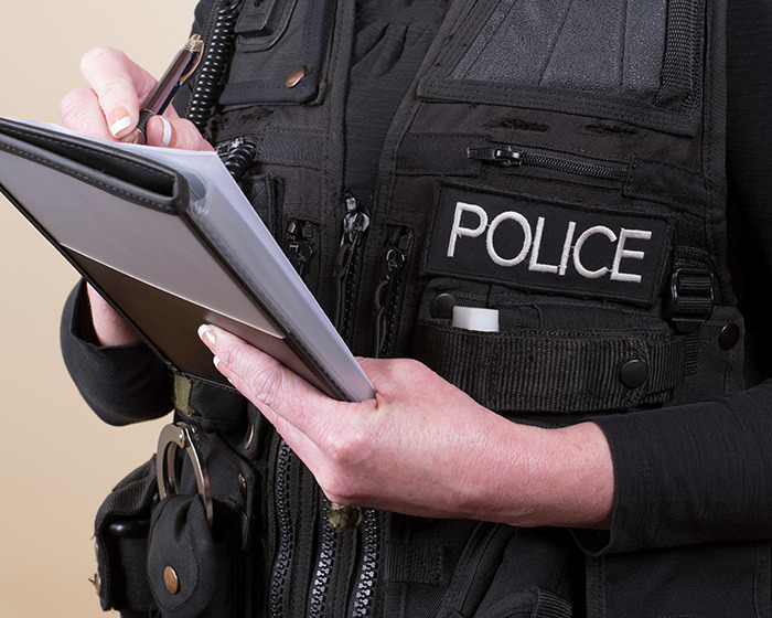 Police officer in uniform taking notes on a notepad related to family dinner arrest involving teen and teacher texts.