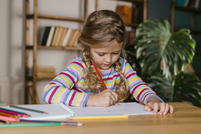 Young girl drawing at a table, illustrating how medical neglect can affect development and daily activities.