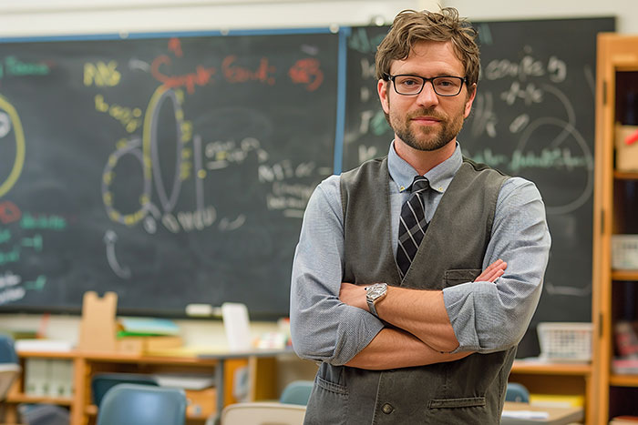 Man upset with unwanted puppy responsibility, standing in a classroom with folded arms and a serious expression.