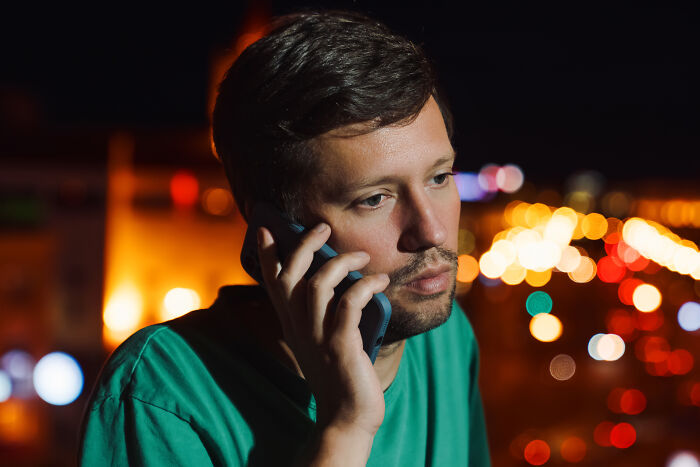 Man in green shirt talking on phone at night, representing strange 911 calls operators received that were true.