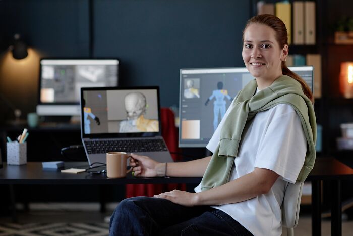 Young woman smiling in front of computer screens showing 3D modeling, representing people who lost jobs to AI.