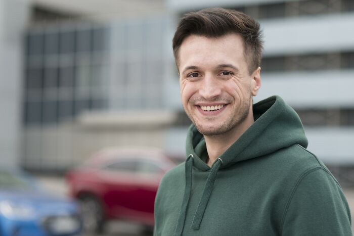 Young man in green hoodie smiling outdoors near parked cars, representing accountants with unexpected lively stories.