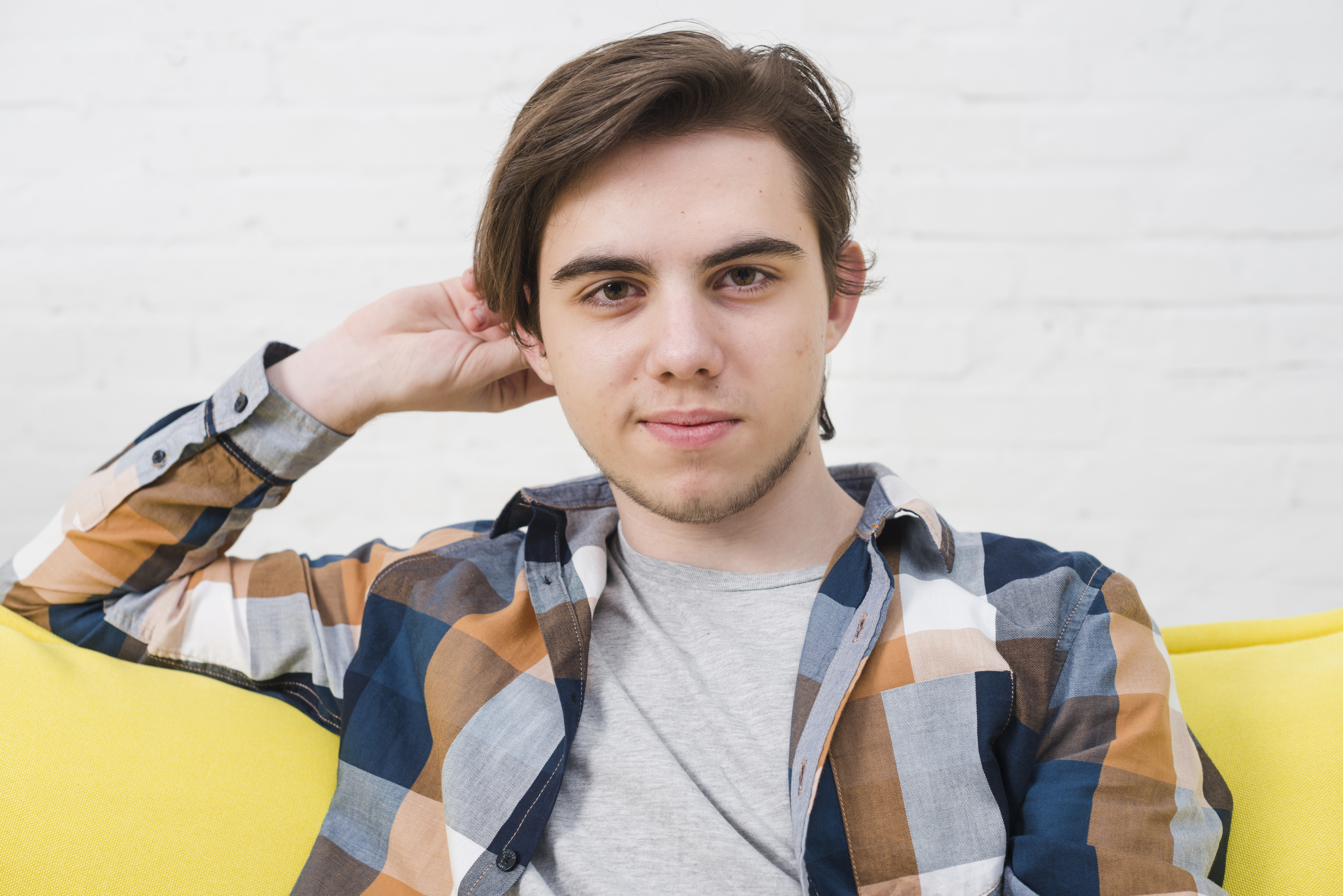 Young man with casual shirt sitting on a yellow couch, symbolizing stepson involved in inheritance family dispute.