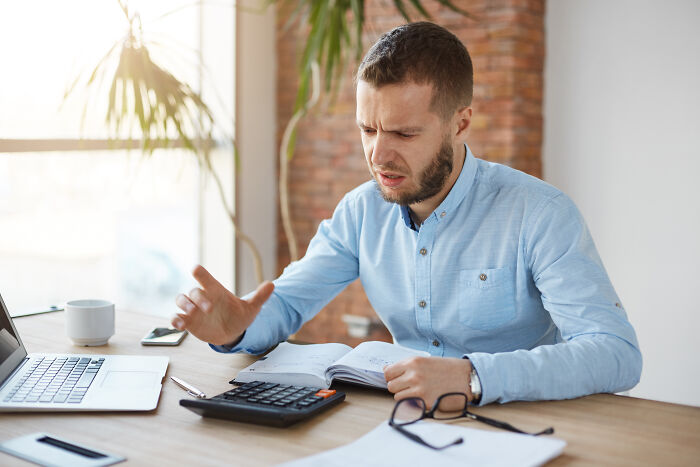 Man in blue shirt using a calculator with documents at a desk, illustrating accountants and crazy stories.