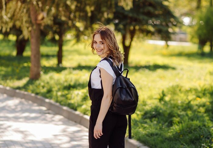 Young woman with backpack smiling outdoors in park, capturing a moment of folks misreading social cues in a lighthearted way.