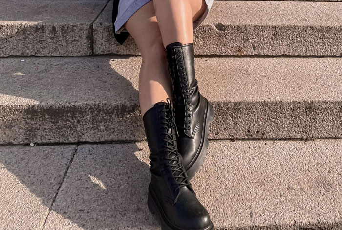 Woman wearing black leather boots sitting on stone steps in outdoor setting showing grandma&rsquo;s shoes.