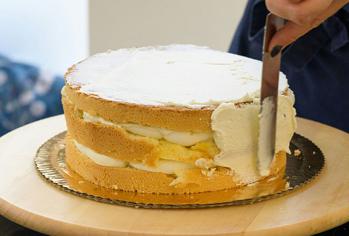 Woman spreading icing on a layered cake, illustrating the perfect delicious bakery revenge scene.