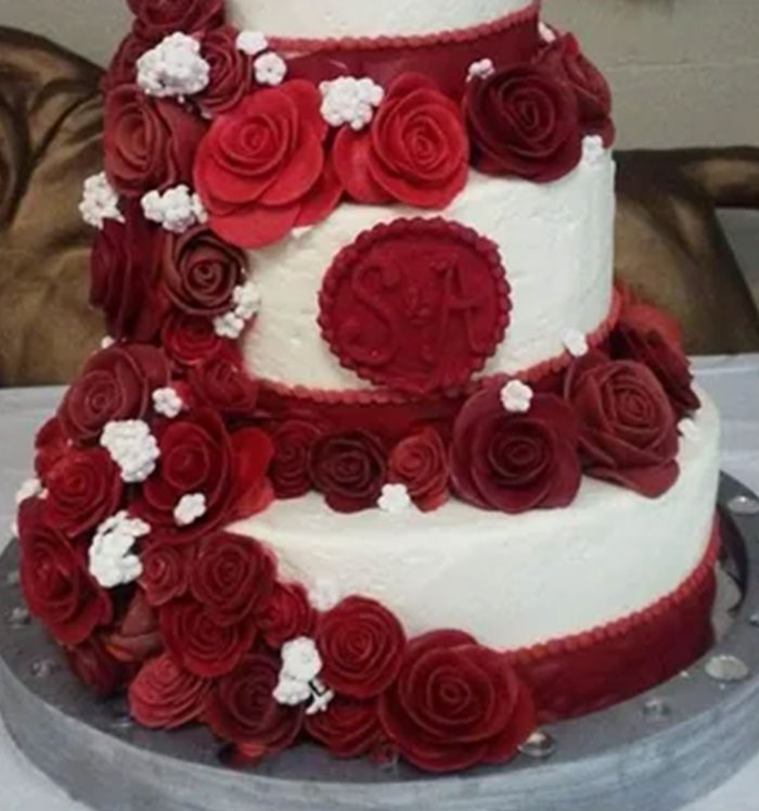 Two-tiered cake decorated with red icing roses and small white flowers, showcasing perfect icing on the cake.