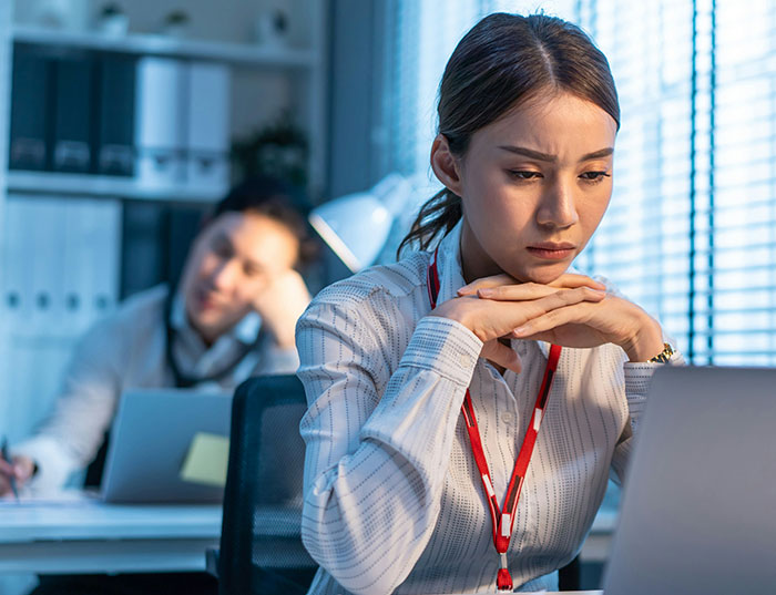 Woman looks frustrated at laptop in office, representing a bakery manager dealing with a challenging situation.
