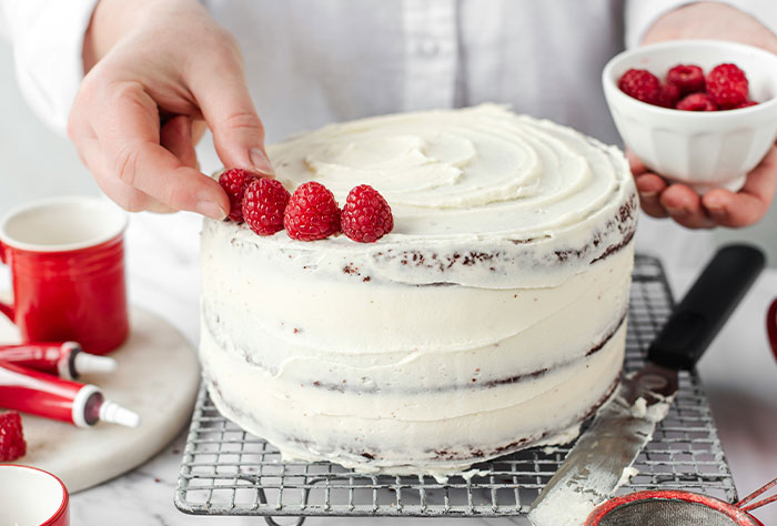 Woman decorating a frosted cake with fresh raspberries, adding the perfect delicious icing on the cake.