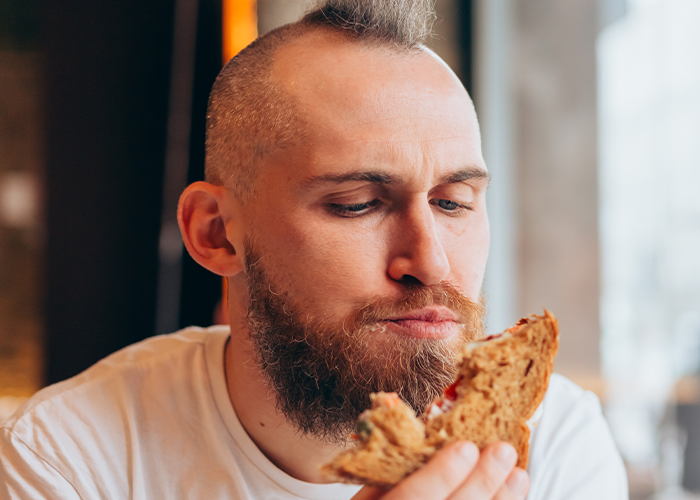 Man with beard eating a sandwich indoors, reflecting the pregnant woman angry husband eats emergency snacks theme. Man with beard eating a sandwich indoors, reflecting the pregnant woman angry husband eats emergency snacks theme.