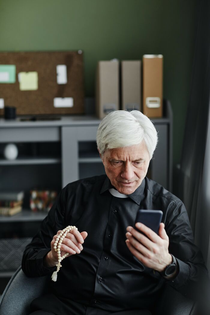 Elderly man holding rosary beads and looking at phone, conveying moments of drunk fumbles and funny fails.