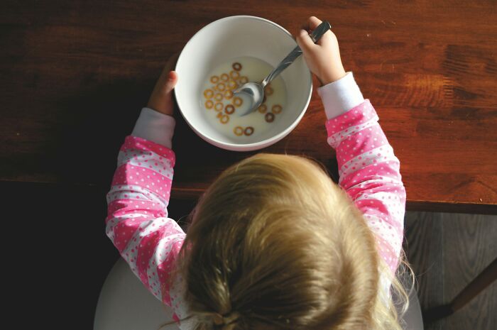 Young child in pink pajamas eating cereal, illustrating childhood rules that impact emotional growth and therapist perspectives.