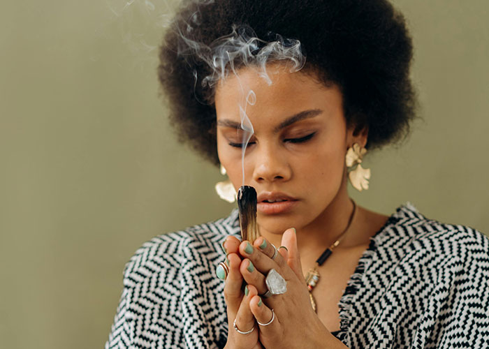 Woman holding smoking sage during a psychic ritual, focusing deeply in a moment of spiritual connection and insight.