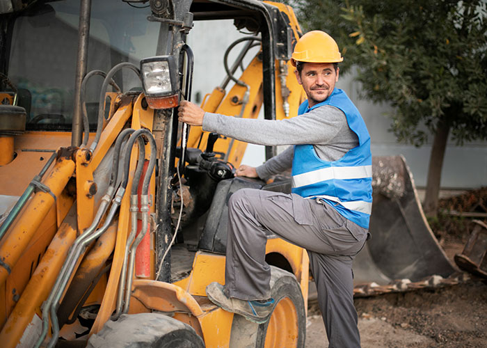 Construction worker wearing a helmet and safety vest operating heavy machinery outdoors on a worksite.