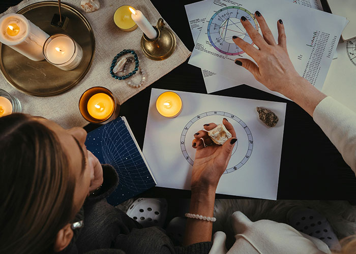 Person holding a crystal during a psychic reading with astrology charts and lit candles on a dark table.