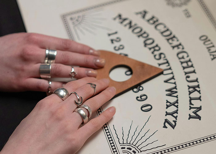 Hands with silver rings using a wooden planchette on an Ouija board, related to psychic predictions coming true.