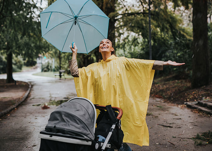 Woman in yellow rain poncho holding blue umbrella and smiling outdoors with stroller on rainy day, linked to psychic predictions coming true.