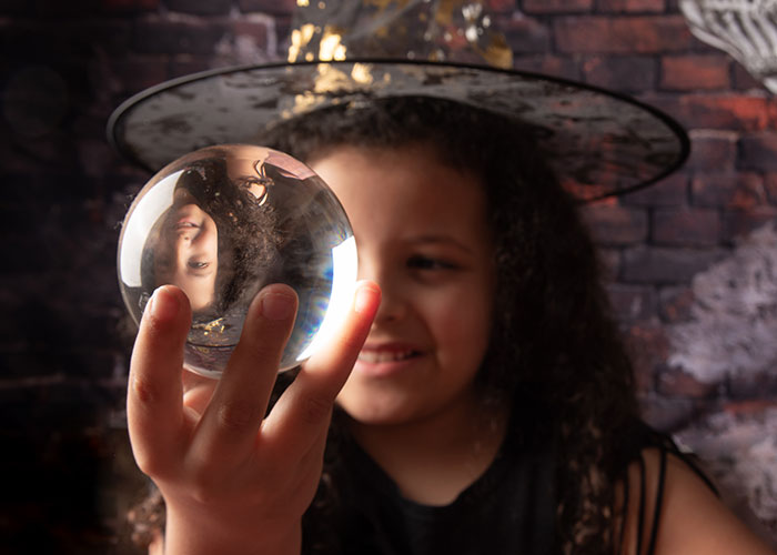 Child wearing a witch hat holding a crystal ball, symbolizing psychic readings and accurate predictions.