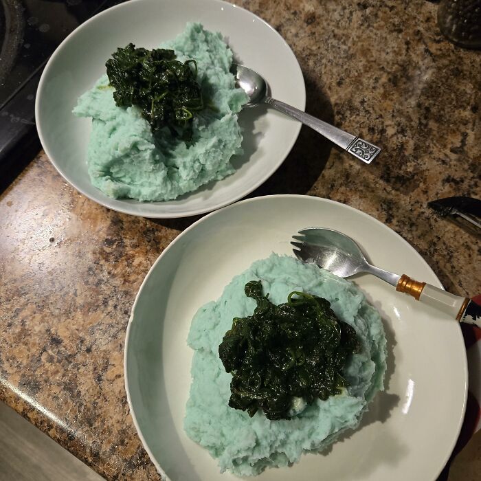 Two bowls of blue mashed potatoes topped with cooked greens on a kitchen counter, a cursed and disgusting food picture.