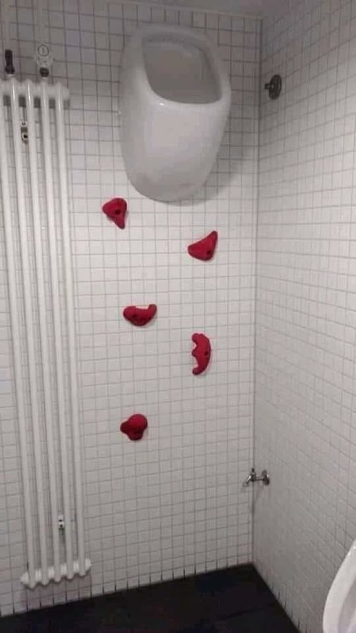 Handroom with white tiles and red climbing holds beneath a urinal, showcasing an out of context pleasures of the occult scene.