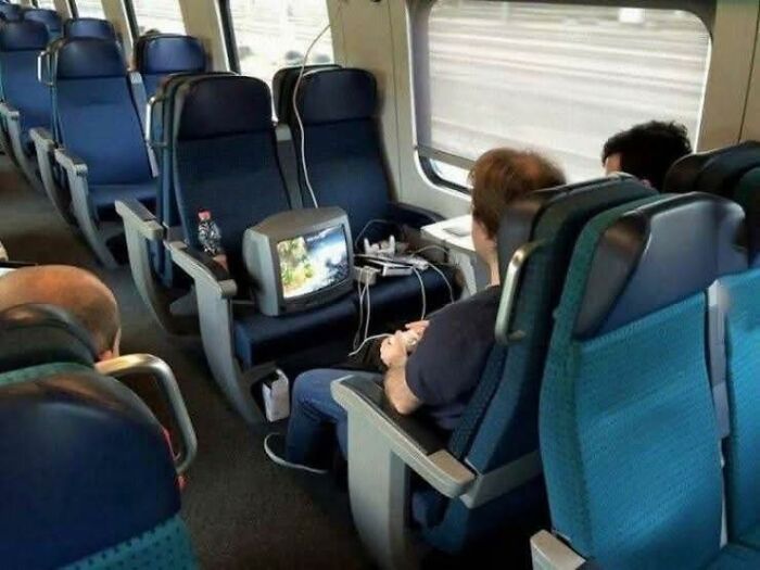 Man playing video games on a retro TV set inside a train cabin, a humorous and out of context occult pleasures moment