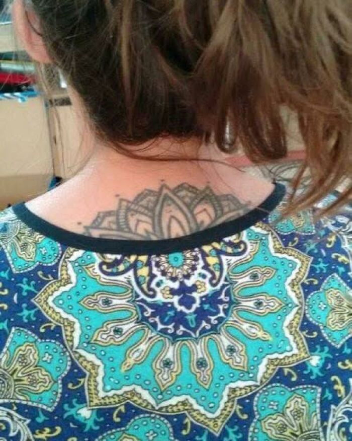 Woman with a mandala tattoo on upper back, wearing a colorful patterned shirt linked to pleasures of the occult theme.